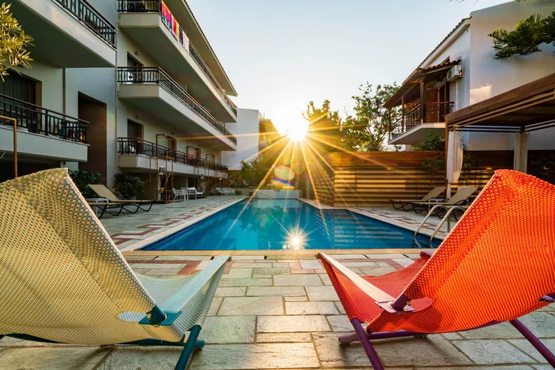 Two loungers by the pool, with the sun low behind the hotel