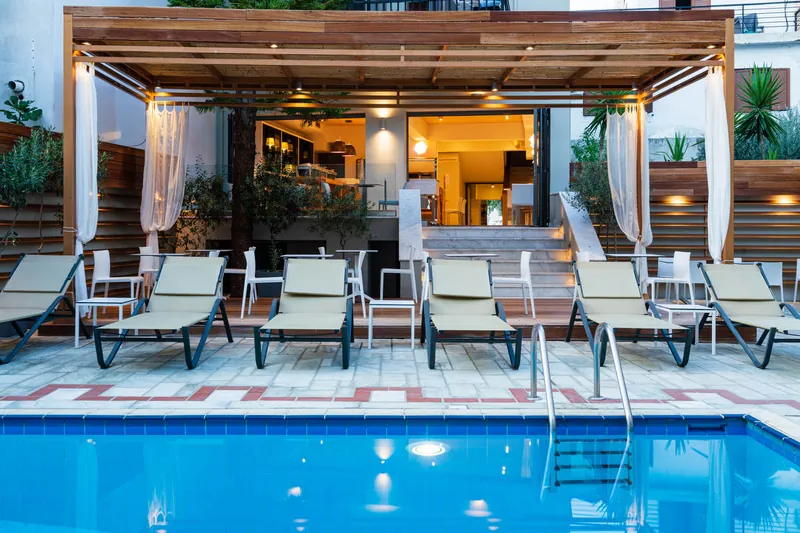 Des transats le long de la piscine, devant la pergola et le bar éclairé