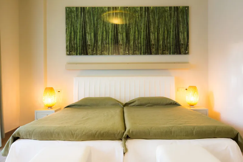 Deux lits simples aux couvre-lits verts sous une image de bambous