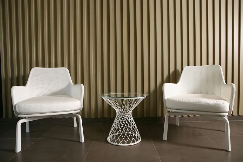 Deux fauteuils blancs et une table en fil métallique contre le mur à lattes